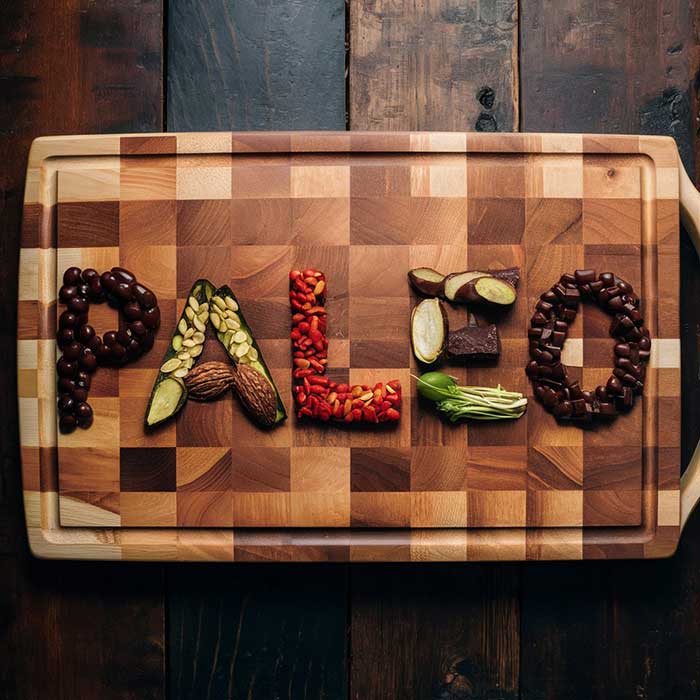 Arrangement of Paleo diet friendly foods on a chopping board including pieces of chocolate to spell the word "Paleo"